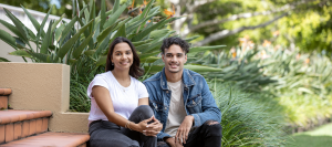 Two students sit on the steps smiling at the camera