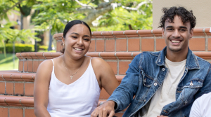 Two students sit on steps smililng at the camera