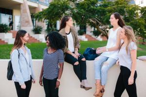 A group of students sit and stand around a wall talking